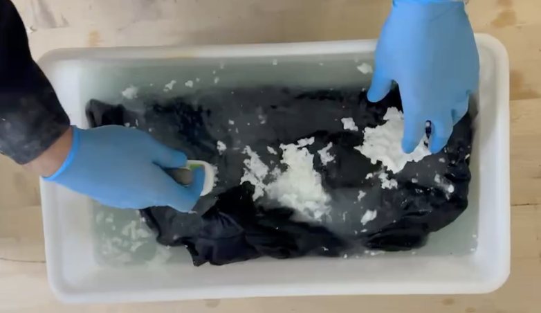 Gloved hands handling foam on a fabric sample during laboratory evaluation